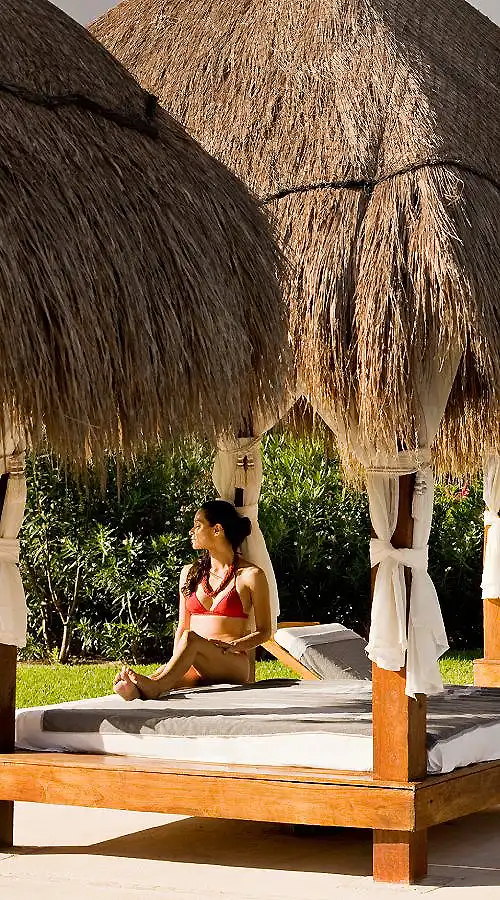 Mujer relaj&aacute;ndose en un catre de resort bajo techo de paja.