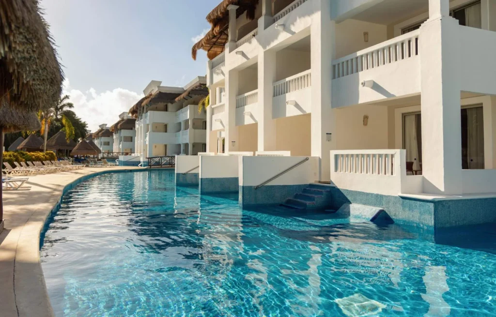 Piscina junto a edificios blancos con balcones y sombrillas de palapa al sol