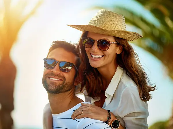 Pareja sonriente con sombrero y gafas en un d&iacute;a soleado de playa