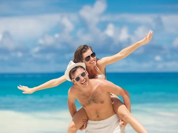 Pareja en la playa, ambos con gafas de sol y toallas blancas, posando