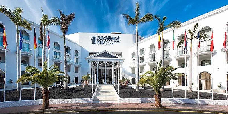 Entrada del hotel Guayaparina Princess con palmeras y banderas al cielo azul