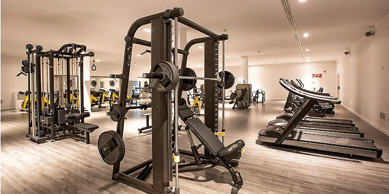 Gimnasio con m&aacute;quinas de pesas, barra y banco de press y cardio.
