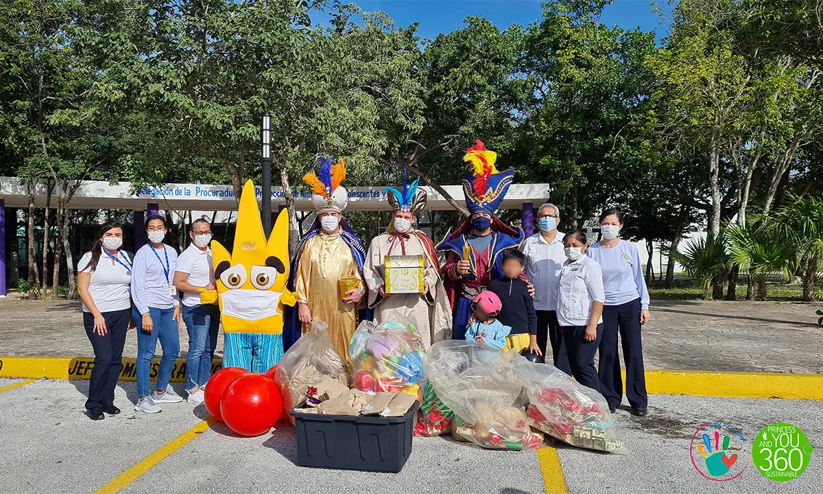 Grupo con m&aacute;scaras y disfraces, entrega de regalos frente a un escenario al aire libre.