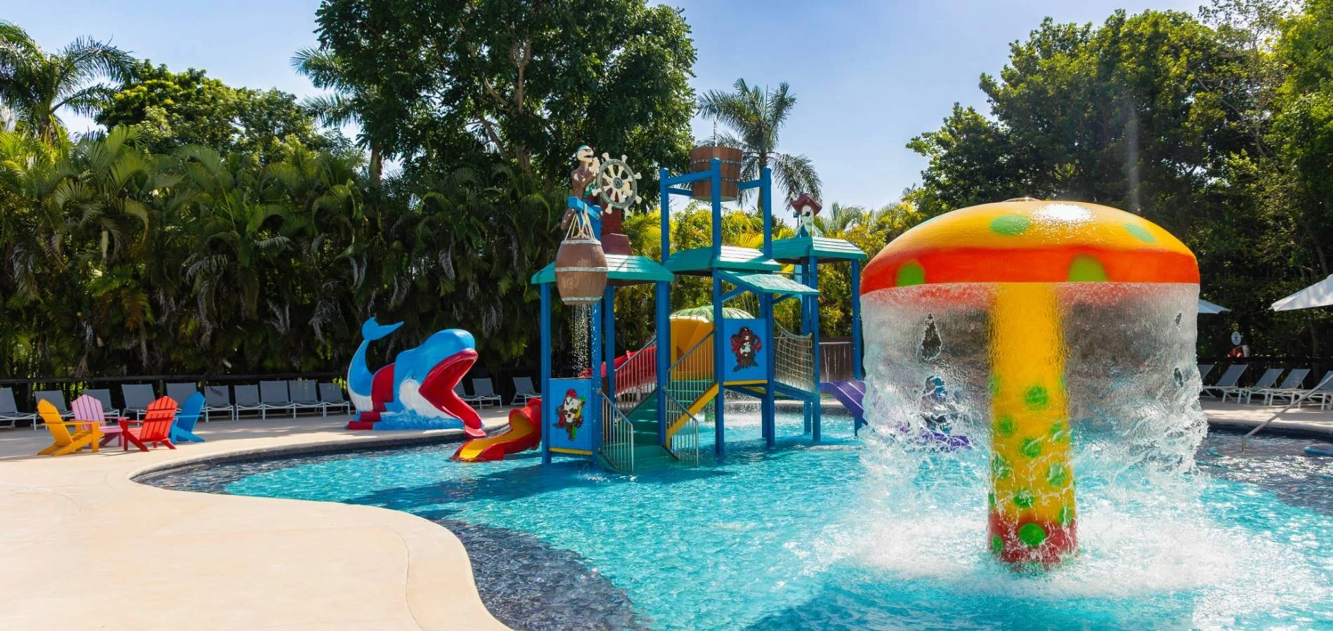Piscina infantil con tanque inflable rojo y tobog&aacute;n, rodeada de palmeras