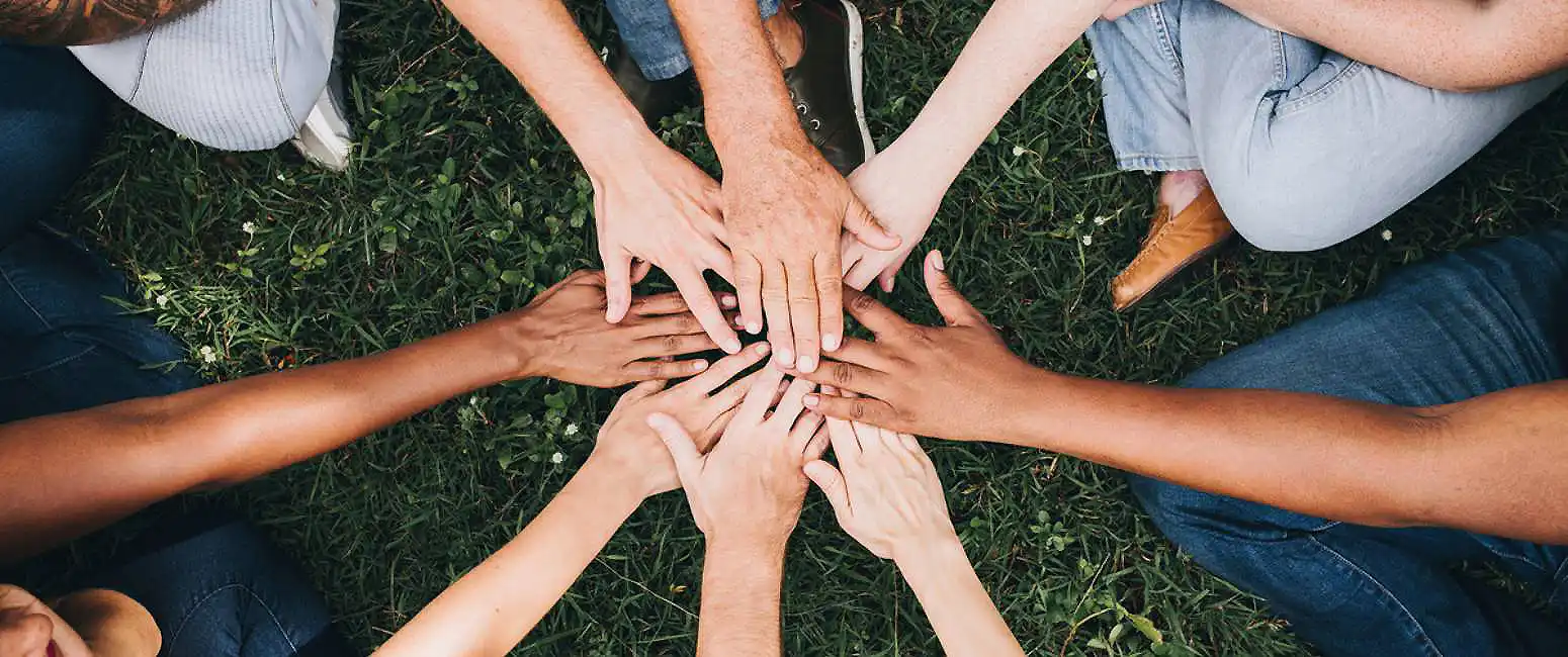 Manos de varias personas formando un c&iacute;rculo sobre el c&eacute;sped, trabajo en equipo