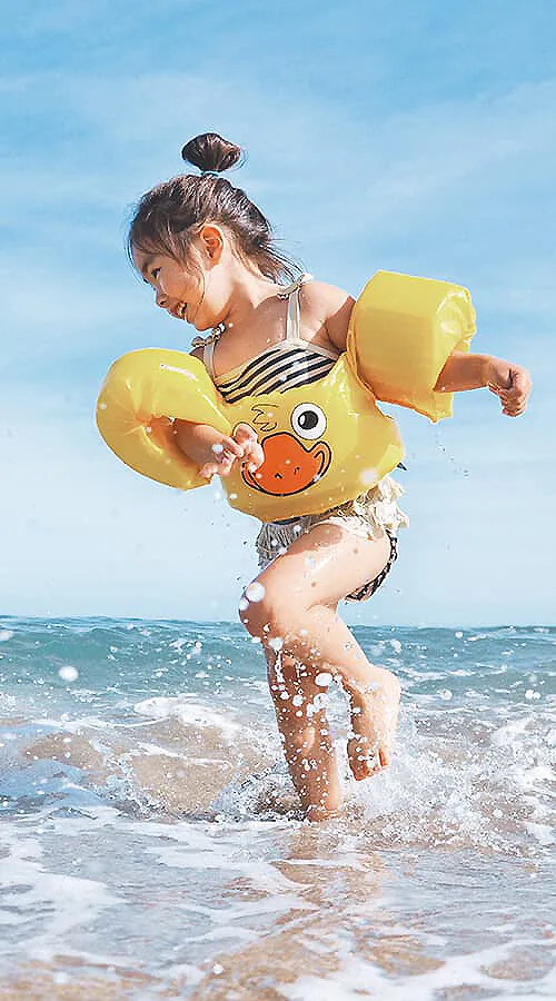 Ni&ntilde;a en la playa con flotadores amarillos, jugando en el agua.