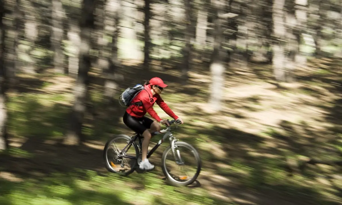 Ciclista con mochila y gorra roja pedaleando por un camino en el bosque