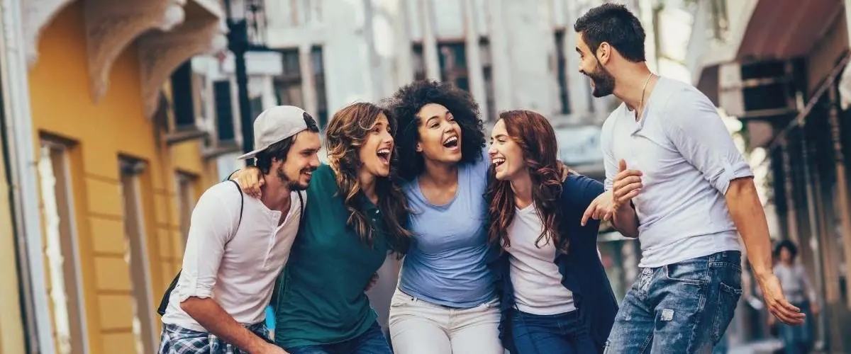 Grupo de amigos riendo y caminando juntos en una calle soleada.