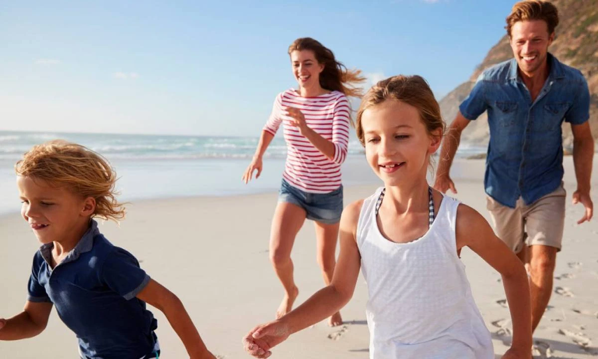Familia jugando en la playa, ni&ntilde;os y adultos corriendo al sol