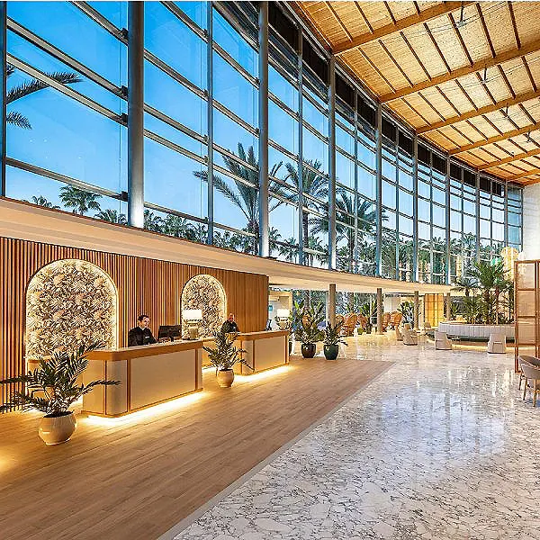 Lobby moderno con recepci&oacute;n, plantas y grandes ventanales azules.