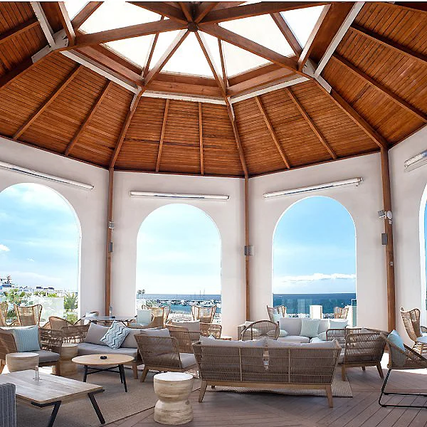 Interior de terraza con techo de madera, arcos y sof&aacute;s frente al mar.