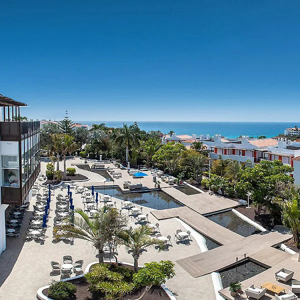Vista de hotel con piscina y jardines frente al mar, bajo cielo despejado.