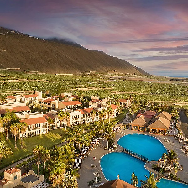 Hotel con piscina azul al pie de monta&ntilde;as y un atardecer sobre el valle.