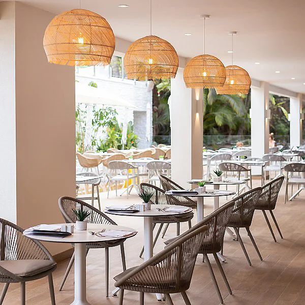 Terraza interior con mesas y sillas, l&aacute;mparas de mimbre y vegetaci&oacute;n.