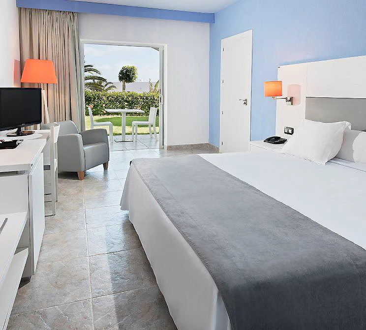Habitaci&oacute;n moderna con cama, sill&oacute;n, TV y salida al jard&iacute;n con terraza.