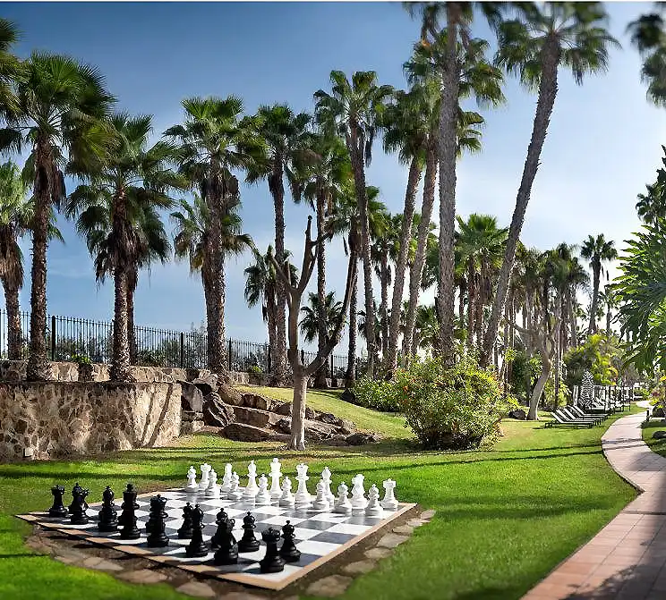 Jard&iacute;n con palmeras y un tablero de ajedrez gigante en el c&eacute;sped.