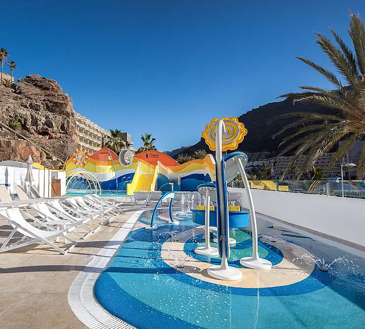 Piscina con toboganes infantiles y palmeras bajo cielo azul en la playa