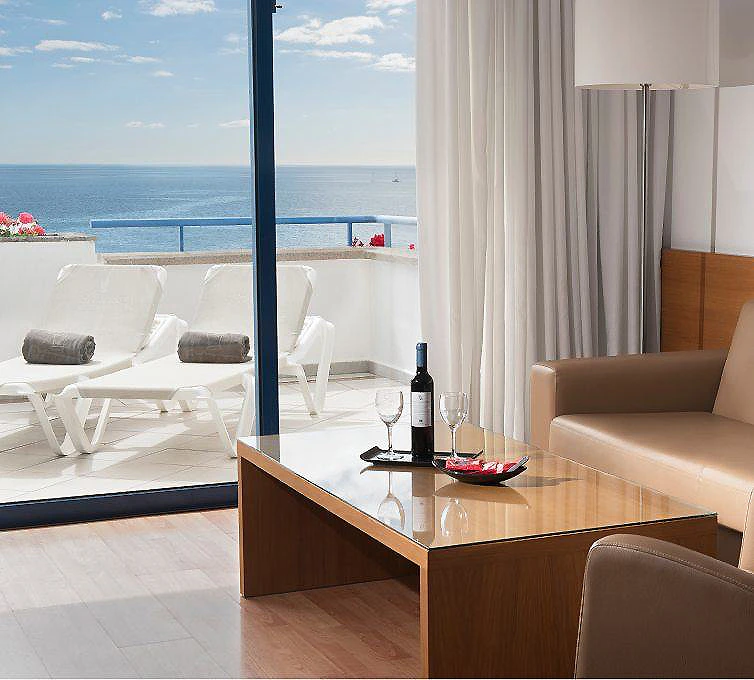 Terraza junto al mar con mesa, sillas y sill&oacute;n de cuero, vista al oc&eacute;ano.
