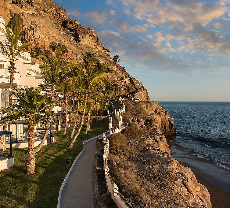 Paseo junto al mar con palmeras, acantilado y edificios frente a la costa