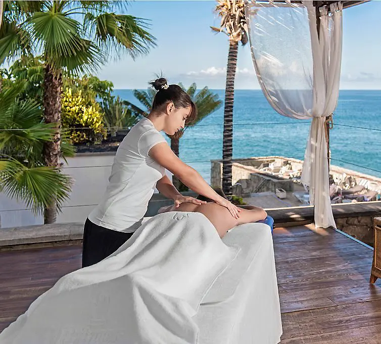 Masajista masajeando a una mujer junto al mar, con palmeras y gazebo