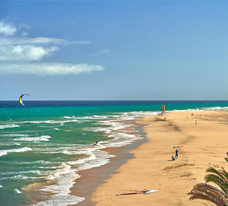 Playa tropical con olas, arena dorada y gente caminando bajo el cielo azul
