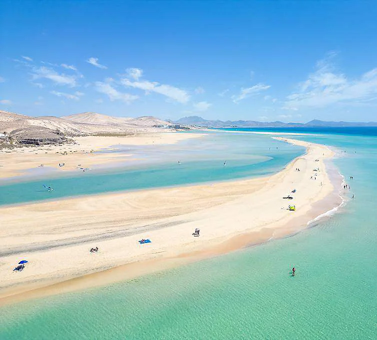 Playa de arena larga con aguas turquesas y barcos, bajo cielo azul.