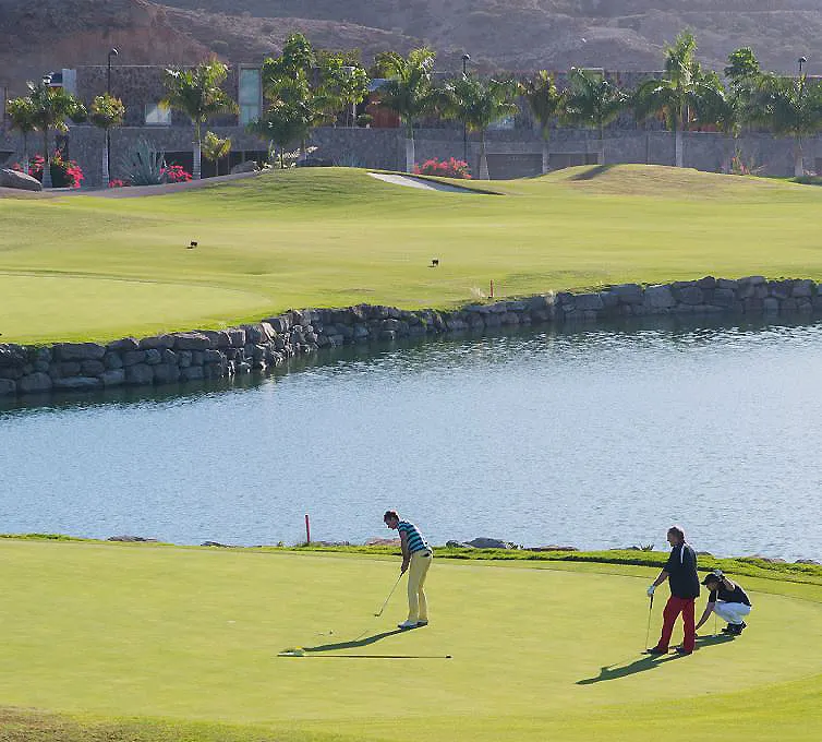 Golfistas juegan en un campo junto a un lago y muros de piedra.