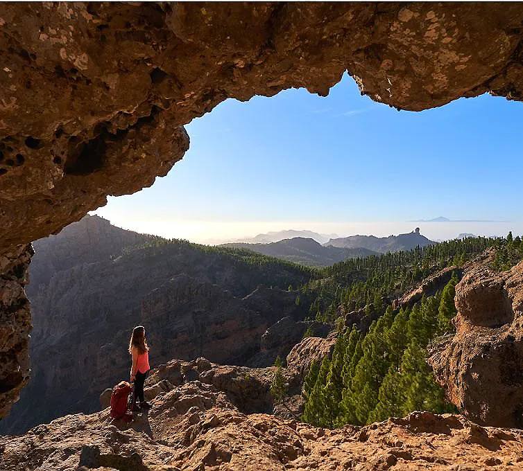 Excursionista en roca, vista de monta&ntilde;as y valle desde una cueva.