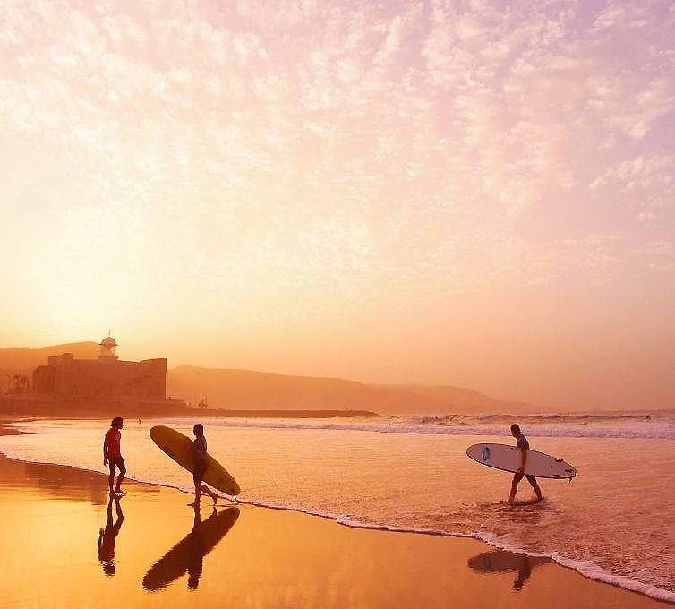 Personas con tablas de surf en una playa al atardecer