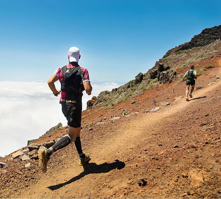 Senderistas subiendo una monta&ntilde;a por un camino de tierra, cielo despejado.