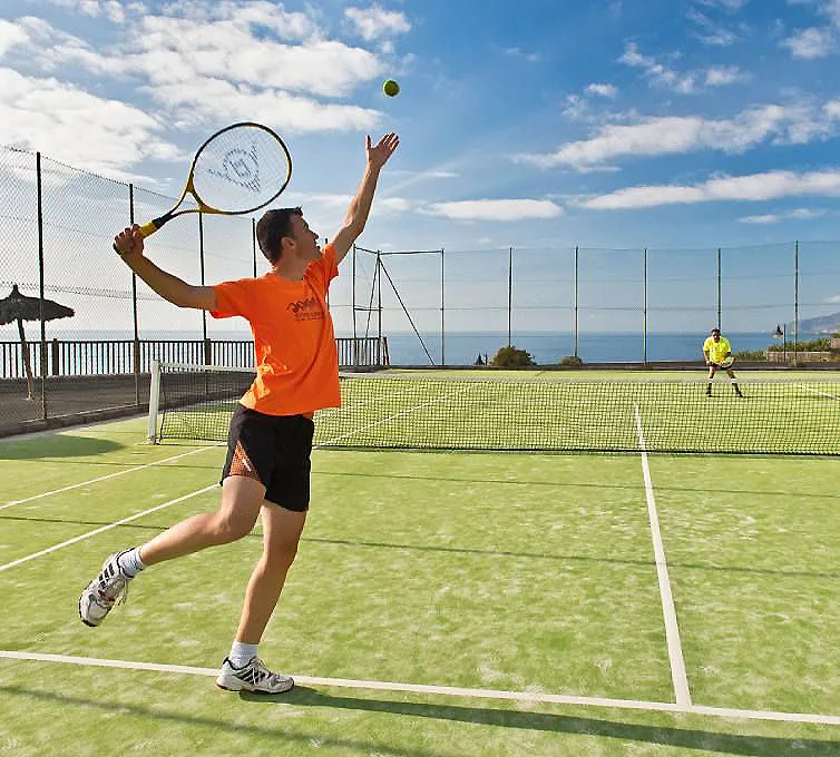 Jugador de tenis lanza una pelota con raqueta en una cancha al aire libre