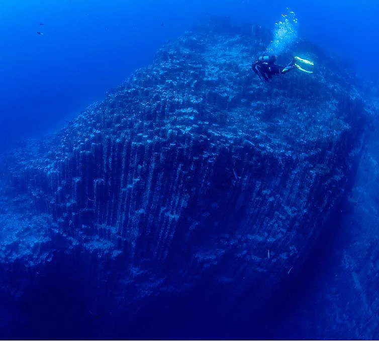 Buceador sobre un arrecife rocoso en aguas azules profundas