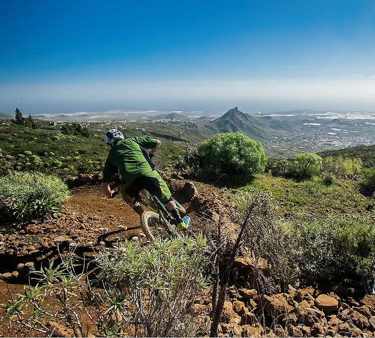 Ciclista de monta&ntilde;a baja por sendero en la ladera con vista panor&aacute;mica