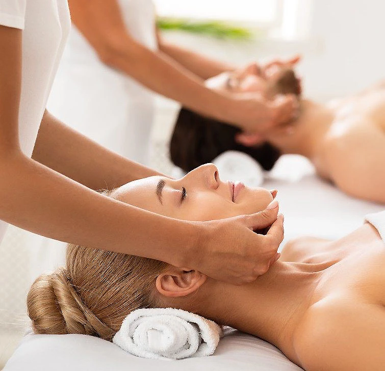 Masaje facial con terapeuta y mujer relajada sobre una camilla blanca