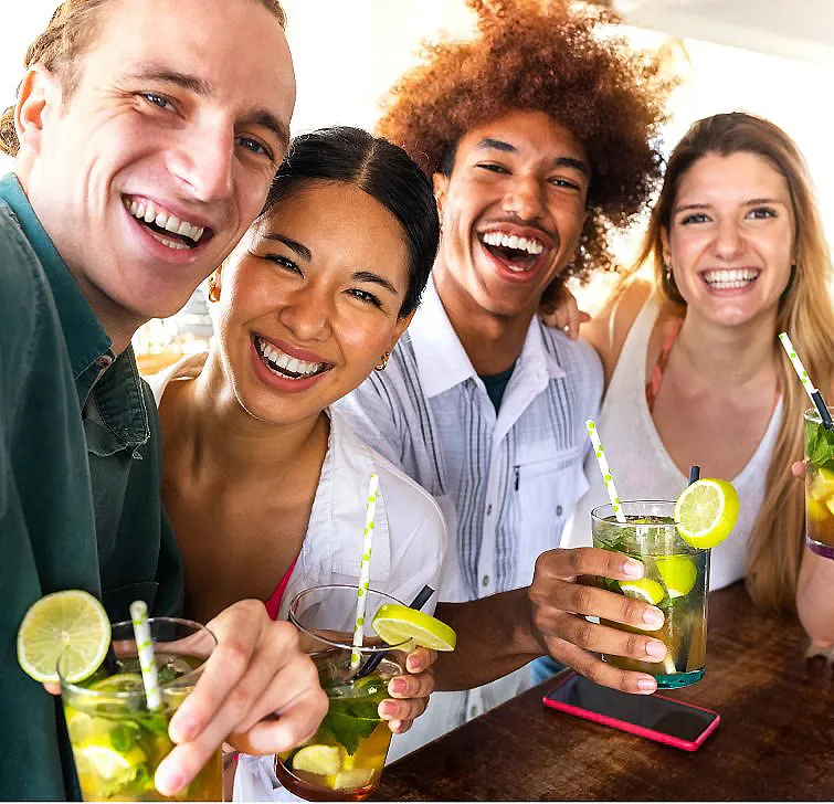 Grupo de amigos sonrientes brindando con bebidas con lim&oacute;n y popotes verdes