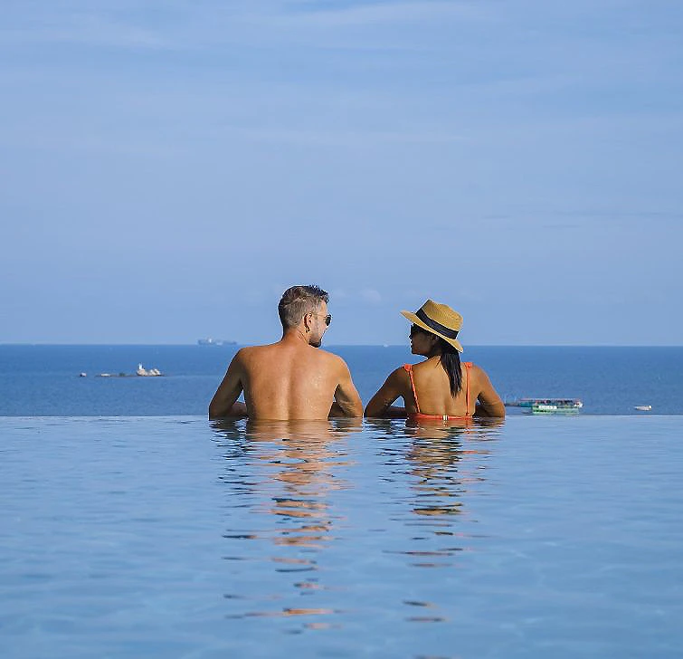 Pareja mirando el mar desde el agua, con barcos al fondo