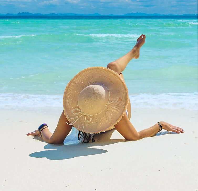 Persona con sombrero sobre la playa, recostada frente al mar.