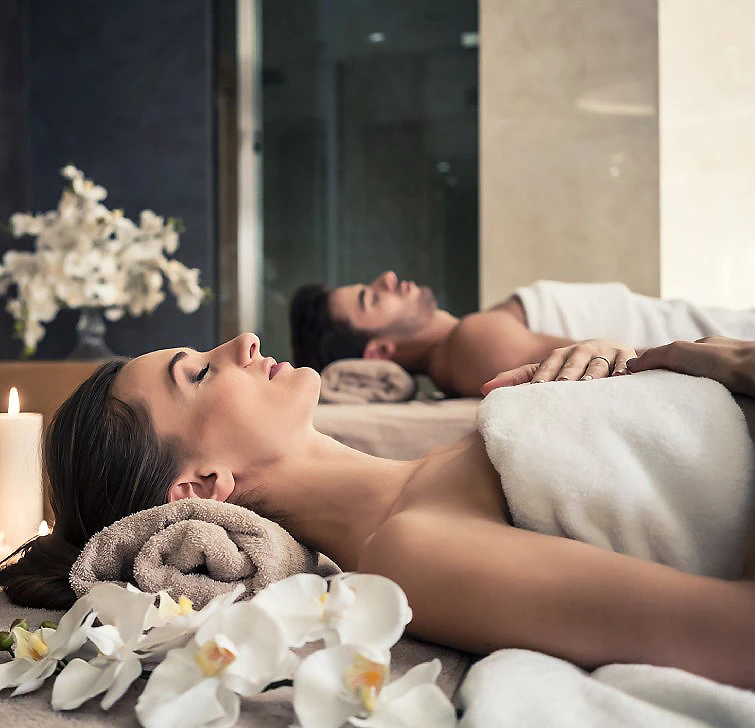 Pareja durmiendo en cama, ella con peluche y flores blancas en primer plano.