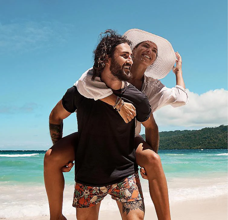 Pareja en la playa con sombrero, abrazados y sonriendo al sol