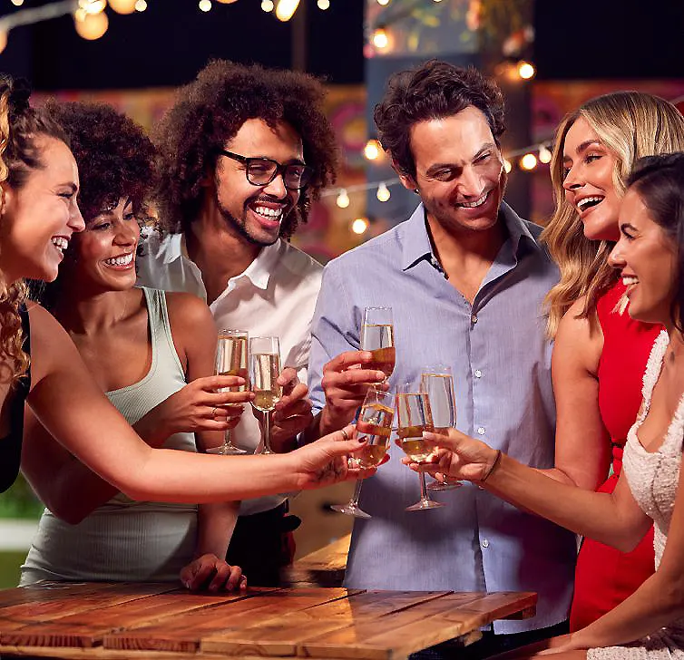 Fiesta de amigos brindando con copas y luces c&aacute;lidas al fondo