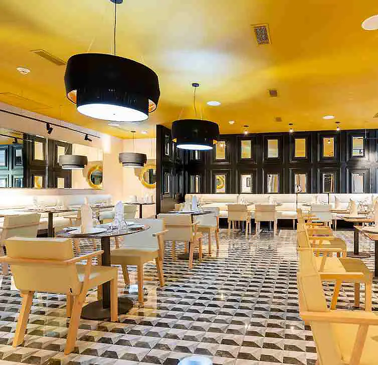 Comedor moderno con mesas y sillas, piso ajedrezado y l&aacute;mparas colgantes.