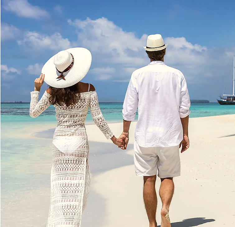 Pareja caminando de la mano en una playa con mar turquesa y cielo azul