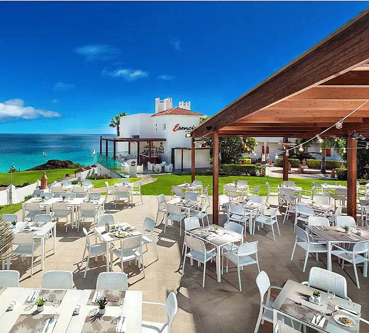 Terraza de restaurante con mesas y sillas, vista al mar y cielo azul.
