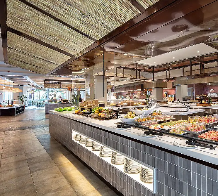 Buffet de desayuno en restaurante con mesas, bandejas de comida y vidrio.