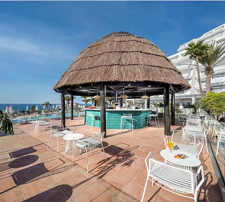 Terraza frente al mar con bar y mesas bajo techo de paja.