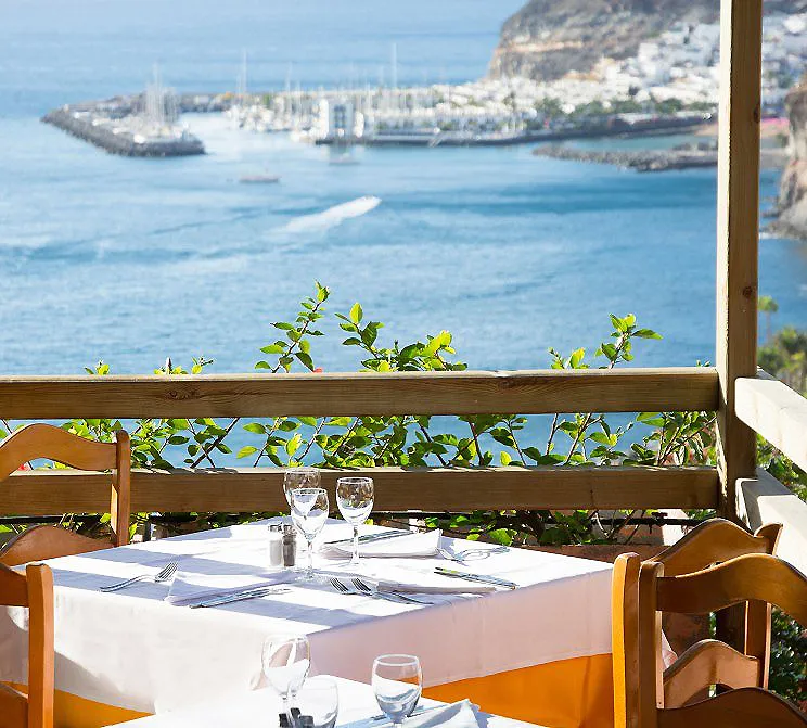 Mesa con manteles y copas en terraza frente al mar y puerto al fondo