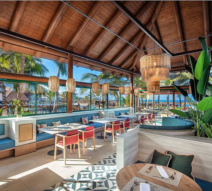 Terraza con muebles de madera, techo de ca&ntilde;a y palmeras al fondo.