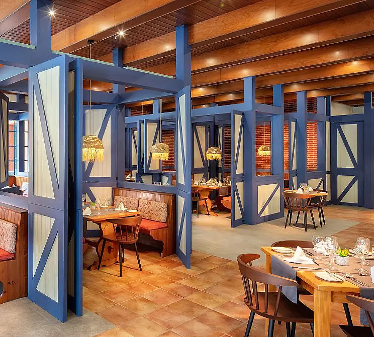 Interior de restaurante con mesas, sillas de madera y pantallas azules decorativas.