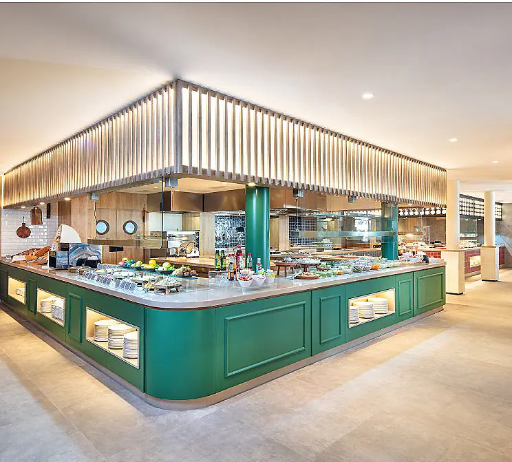 Buffet de hotel con mostrador verde y comida, en comedor luminoso