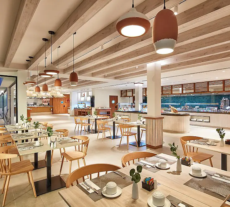 Interior de cafeter&iacute;a moderna con mesas, sillas de madera y l&aacute;mparas colgantes